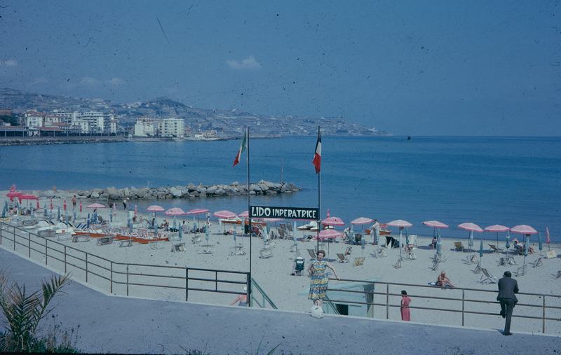 Historische Aufnahme eines Strandes mit rosa Sonnenschirmen und dem Schild „Lido Imperatrice“ bei Sanremo
