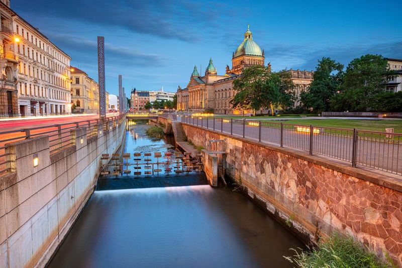 Building with a green dome beside a canal in Leipzig at dusk